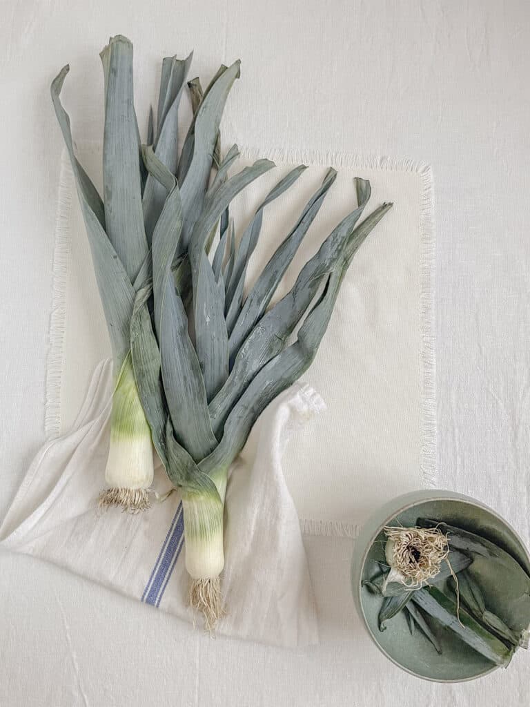 leeks on the table with a white tablecloth and cream napkin nearby.