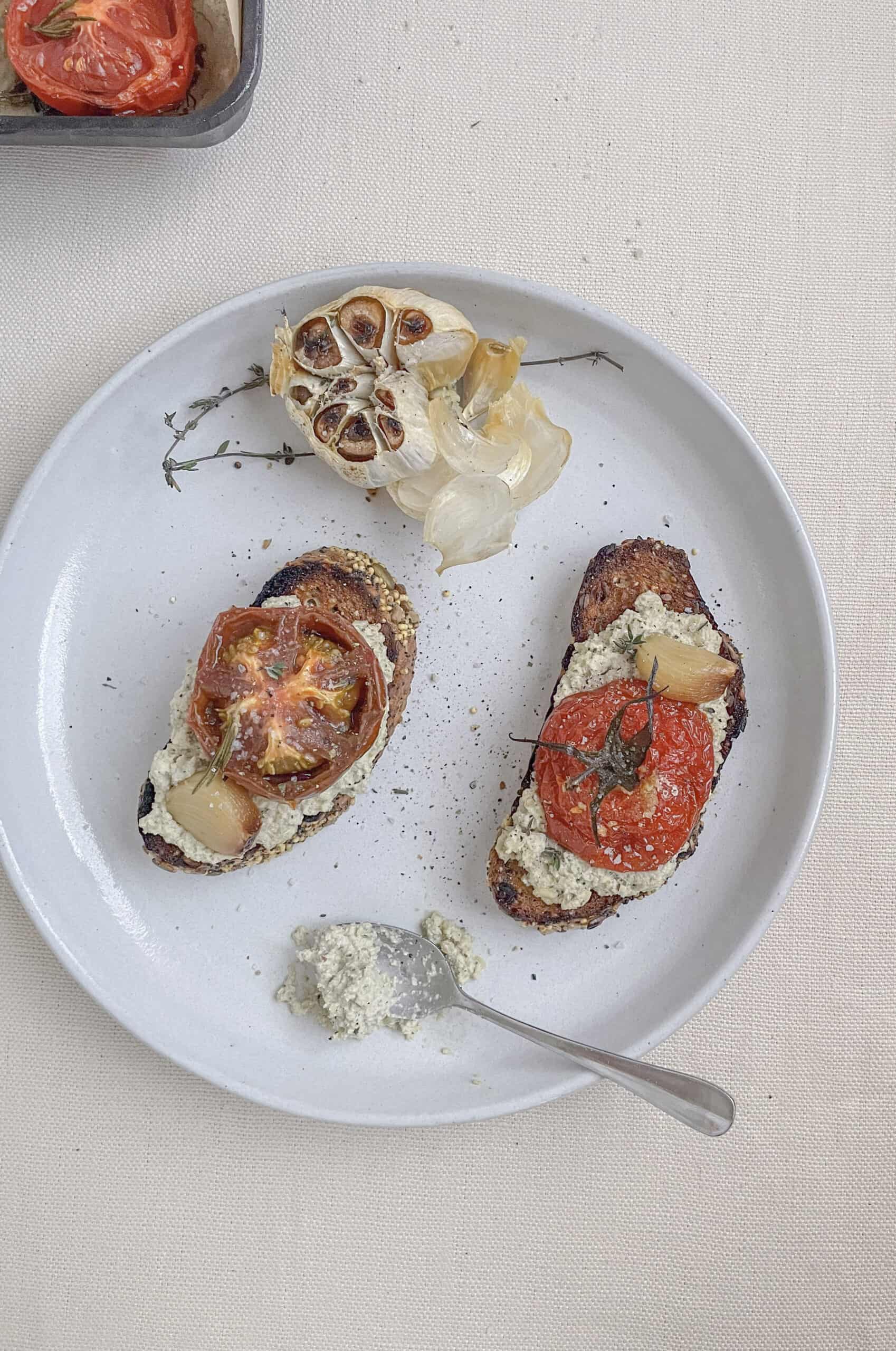 roasted garlic and tomatoes a small plate with toast on a table with a white table cloth.